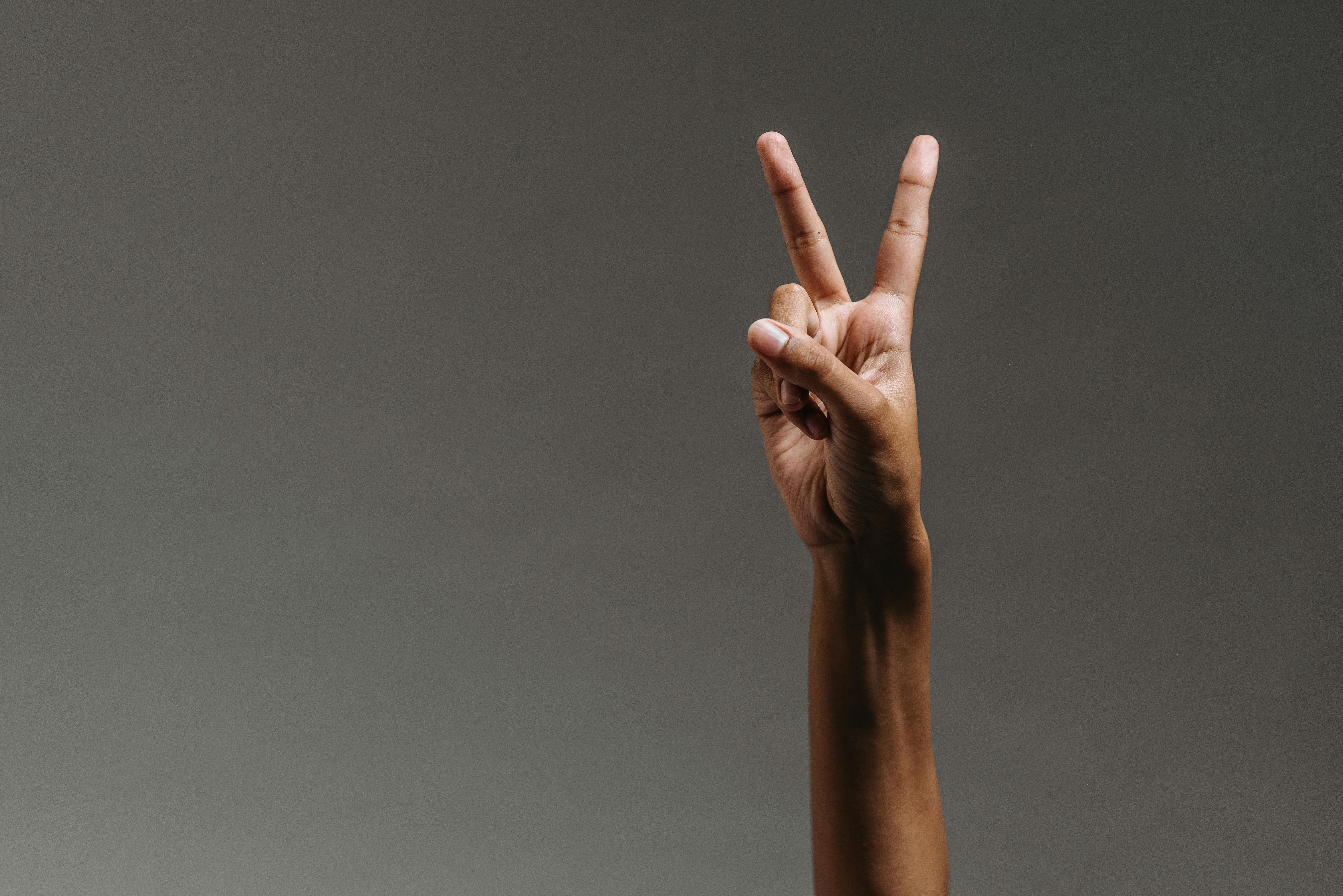 Person's hand raised against a neutral background, making a peace sign with two fingers extended